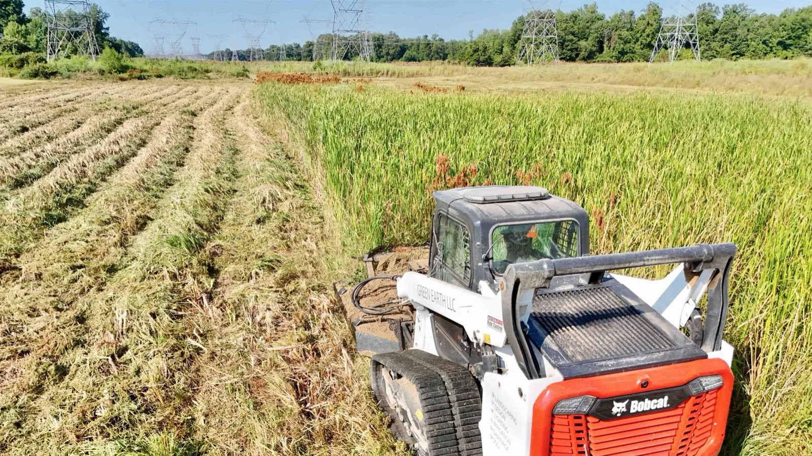 Tracked skid steer bush hogging a field of tall overgrown grass and brush