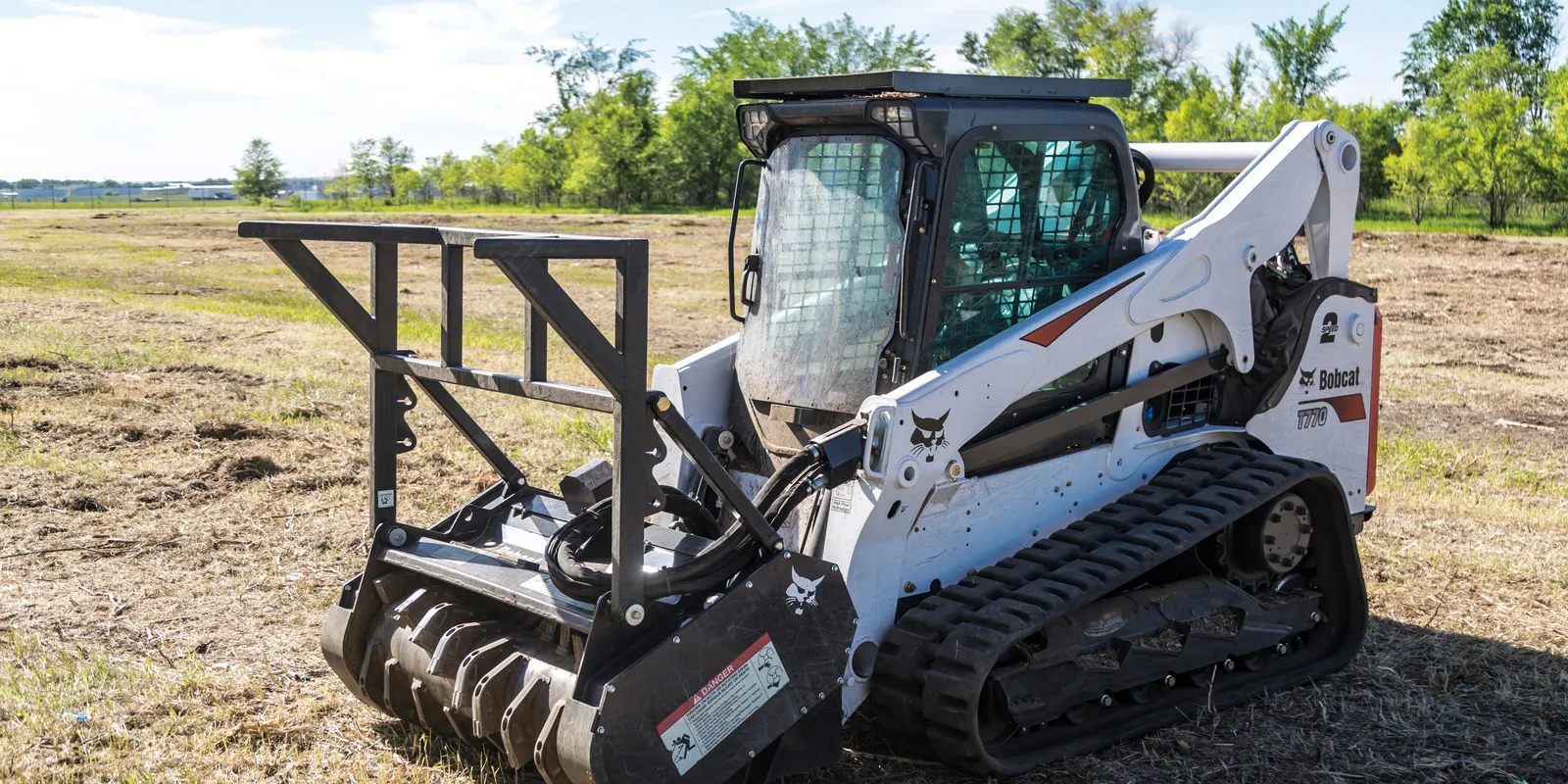 Tracked skid steer with a mulcher head parked on freshly mulched open ground