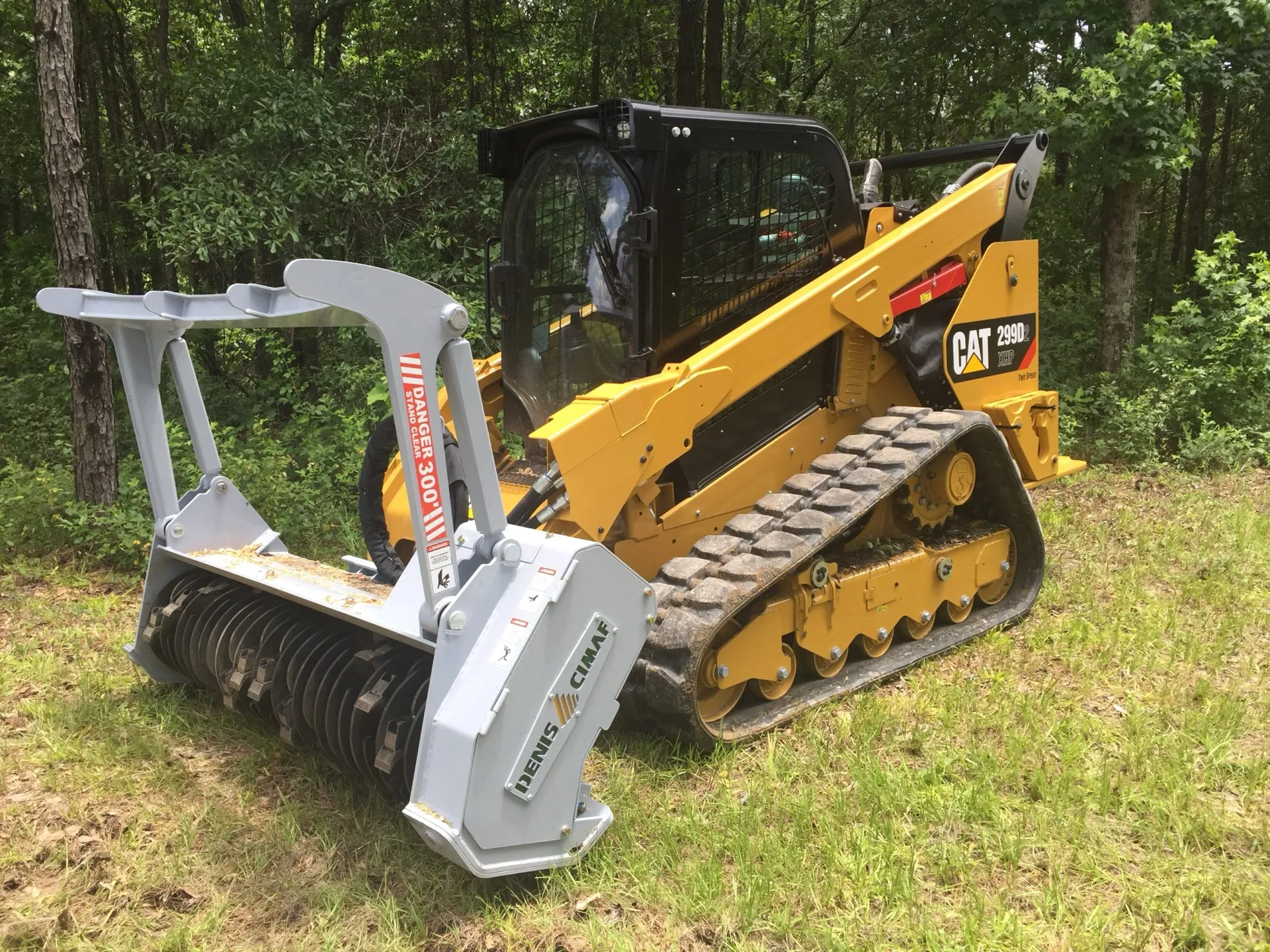 Skid steer with a forestry mulcher head grinding brush at the edge of a wooded lot