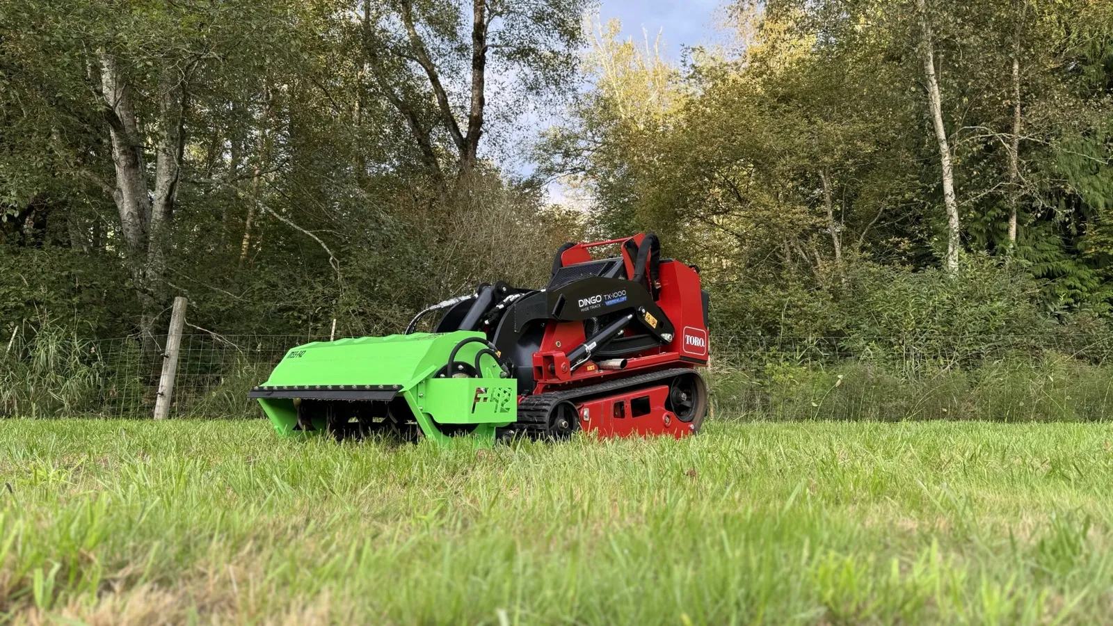 Mini skid steer with a rotary brush cutter working an overgrown field